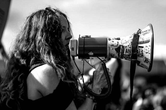 selective focus photography of woman wearing black cold-shoulder shirt using megaphone during daytime